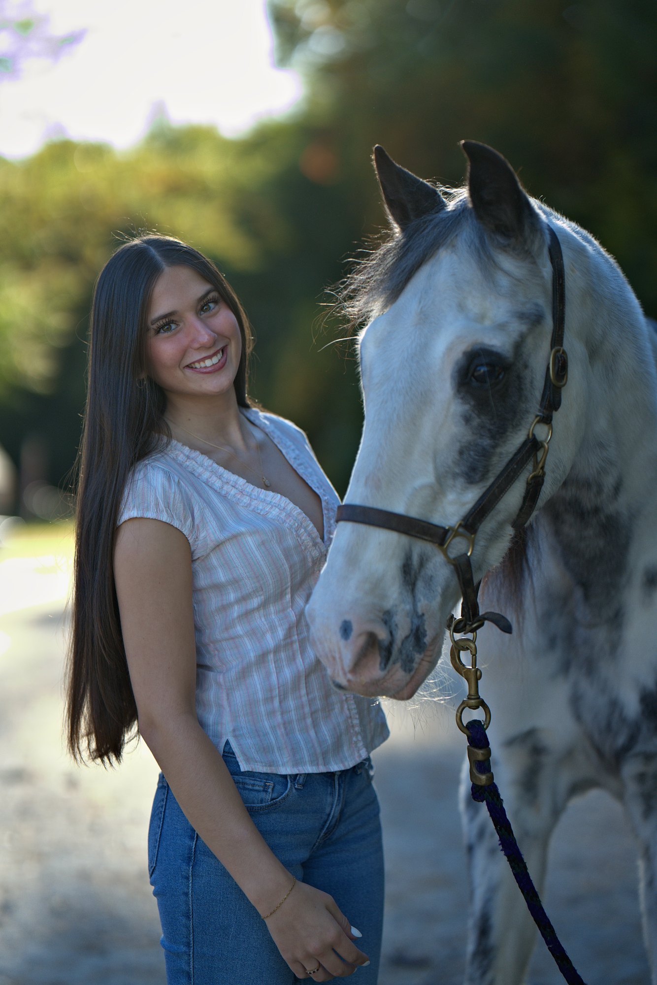 Smiling young woman with long dark hair standing beside a dappled grey horse